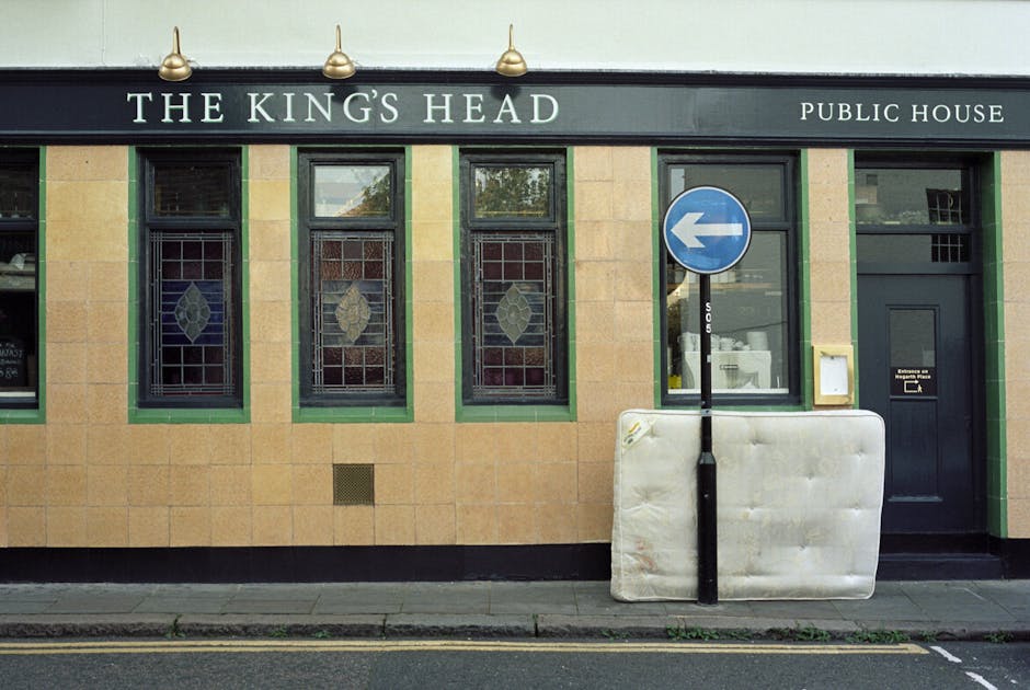 The exterior of a pub named 'The King's Head' features a façade made of light brown sandstone tiles with green-painted window frames and detailing. Four rectangular windows with decorative stained gl